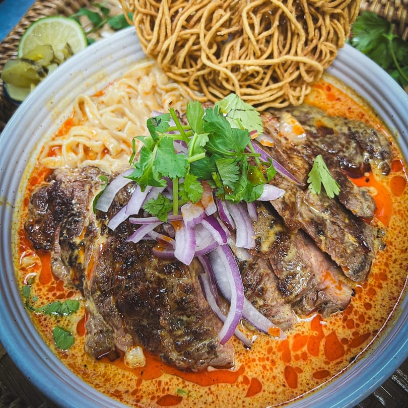 Jumpa Lao Thai Bistro's Khao Soi with grilled steak, noodles, red onions, and cilantro in a rich curry broth.