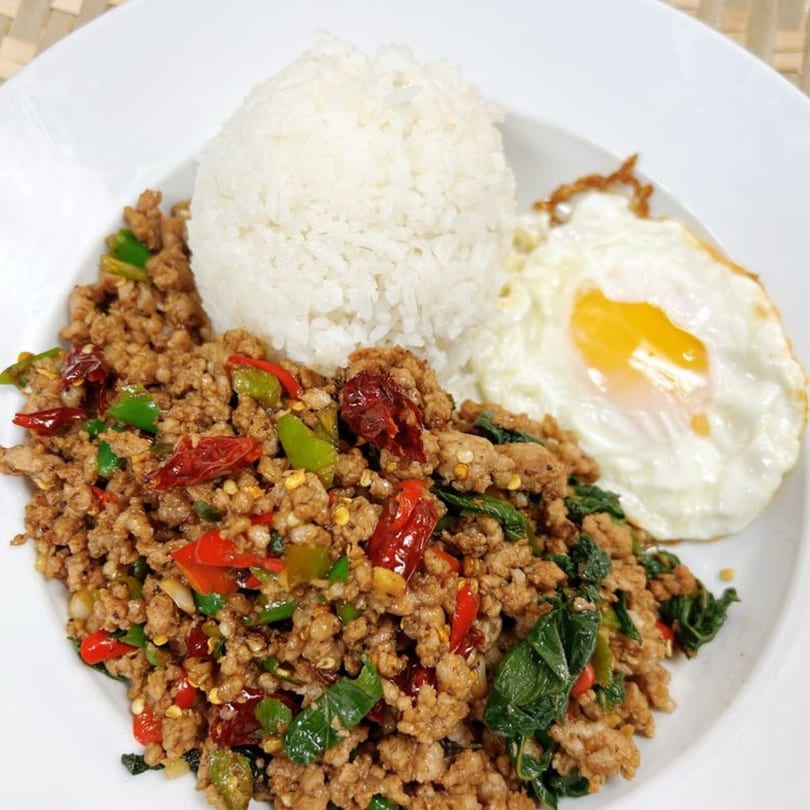 Thai Basil Chicken with rice and a fried egg on a white plate.