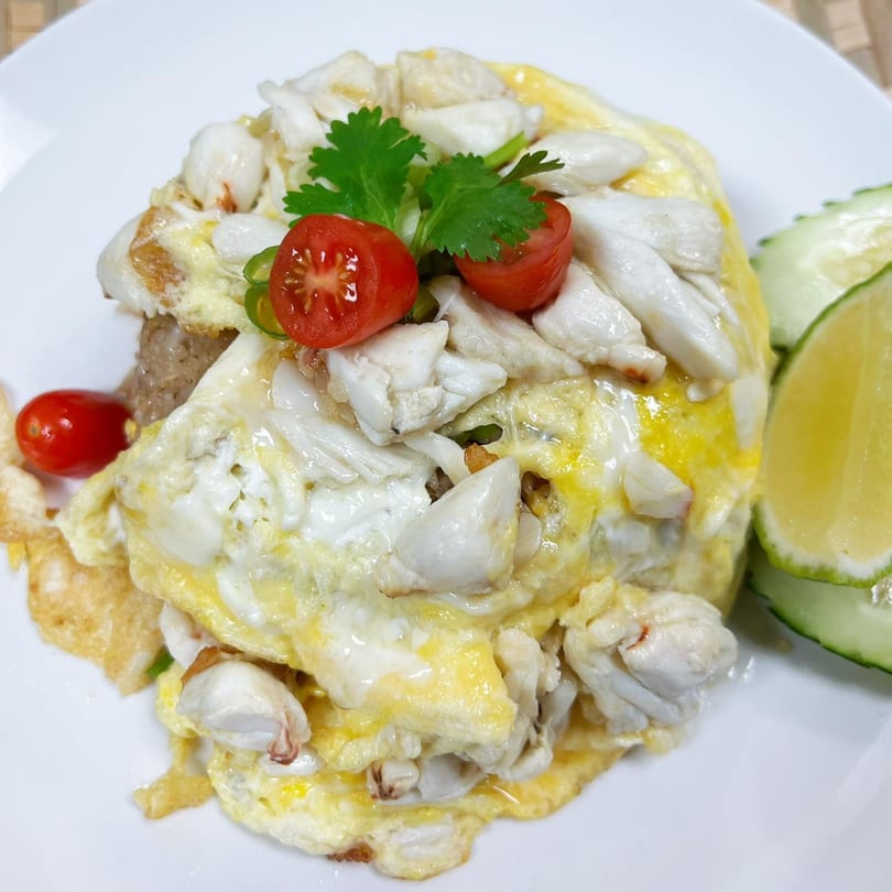 Thai crab omelet with cherry tomatoes, cilantro, cucumber slices, and a lime wedge on a white plate.