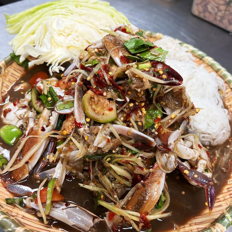 Spicy Thai papaya salad with blue crab, noodles, and cabbage on a woven plate.